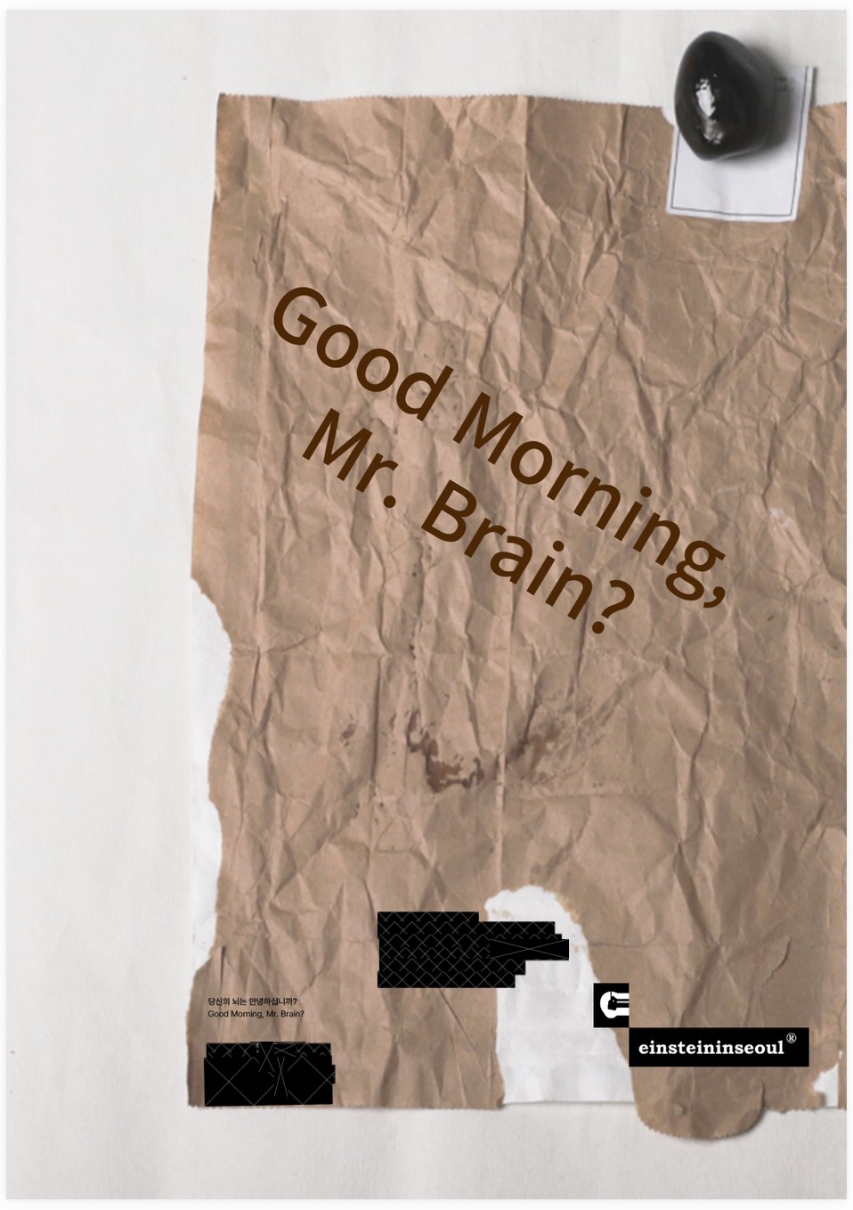 Good Morning, Mr. Brain? 포스터 — 구겨진 갈색 종이에 얹힌 검은 돌
